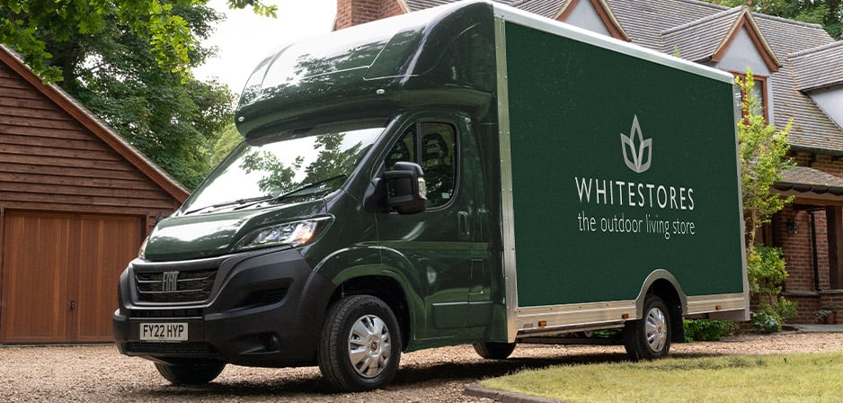 A green White Stores delivery van parked outside a house.