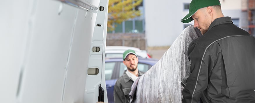 Two delivery men taking a sofa delivery out the back of a van.