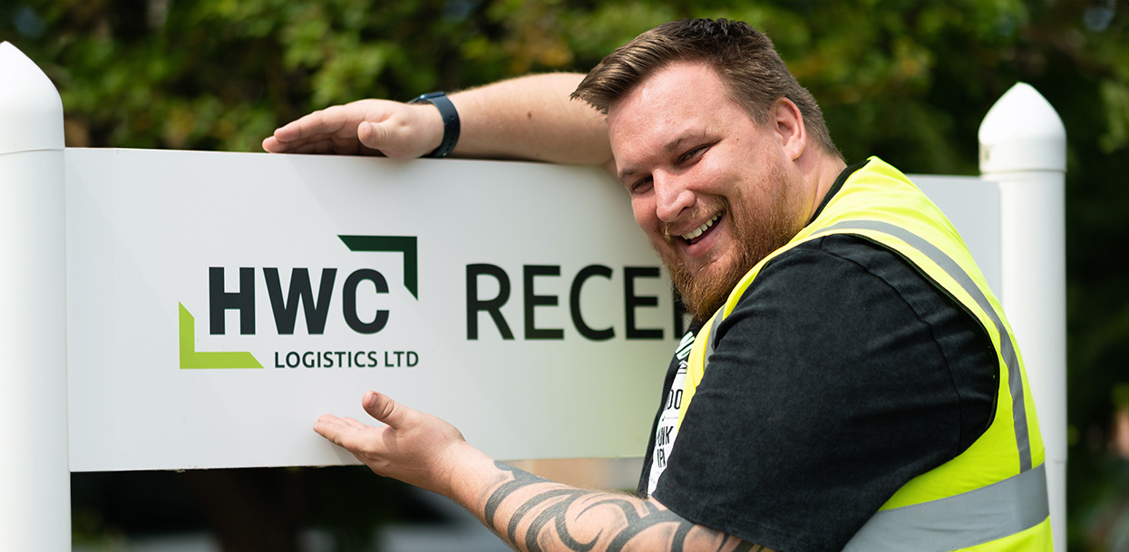 Headshot of a HWC Logistics Ltd employee next to the company sign.